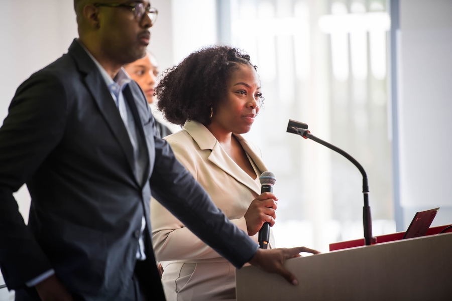 Denzil Streete leans on a lectern while Noelle Wakefield speaks from behind it