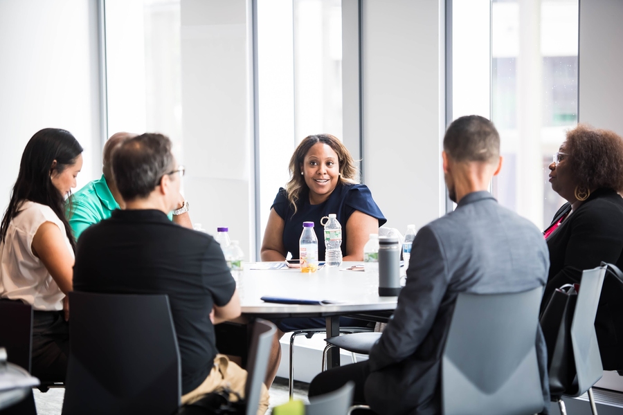 A diverse group of 6 people sit at a round table by a window