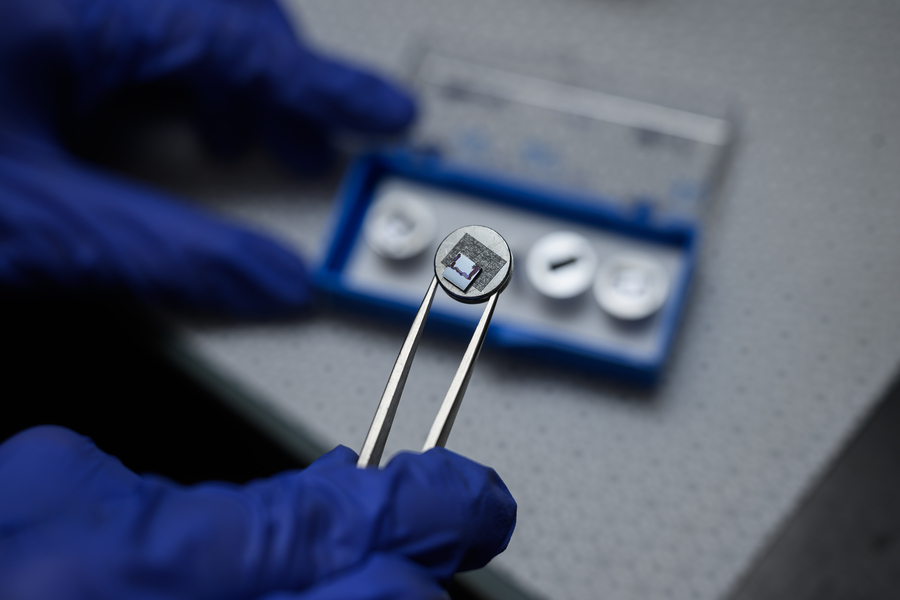 Close-up of a gloved hand holding a dime-sized disk with tweezers