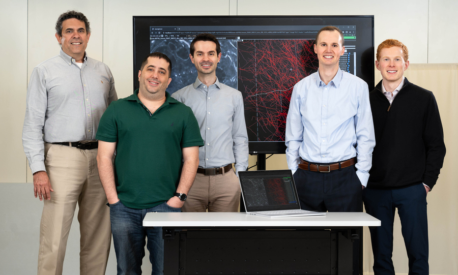 Five NeuroTrALE team members stand in front of a projector showing a demo of the software.