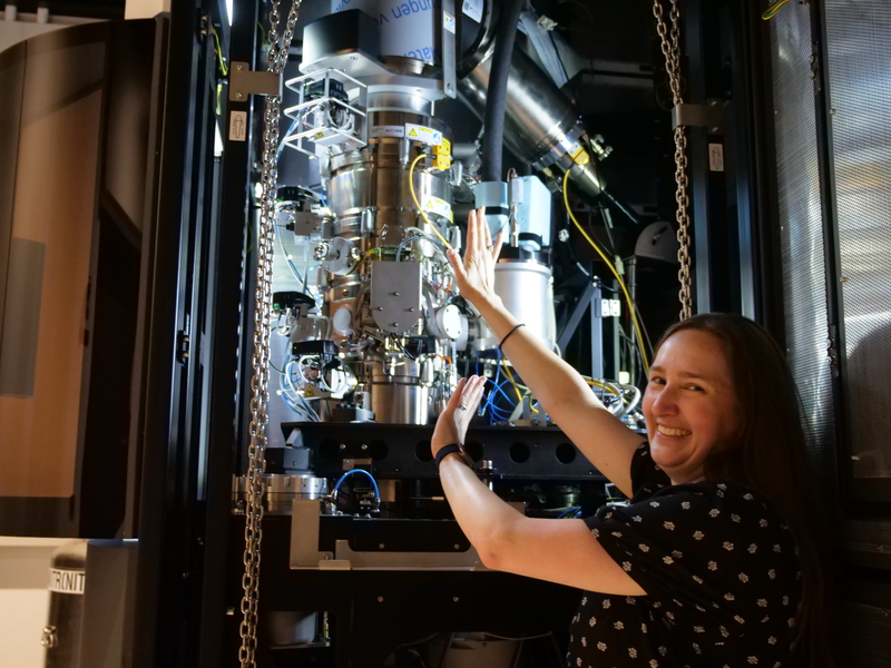 Sarah Sterling, smiling, next to barrel-shaped microscopy equipment
