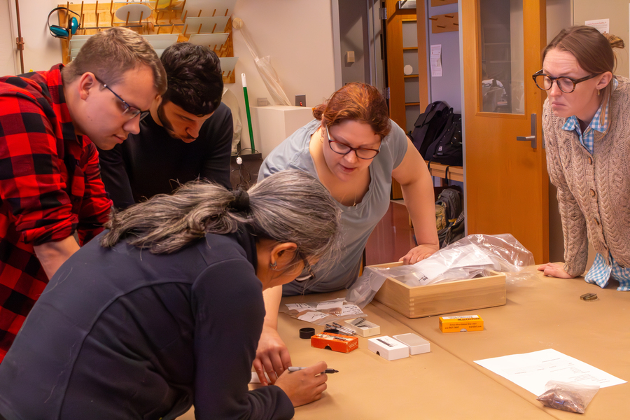 An MIT instructor and students huddle around a table, examining something the camera can’t see