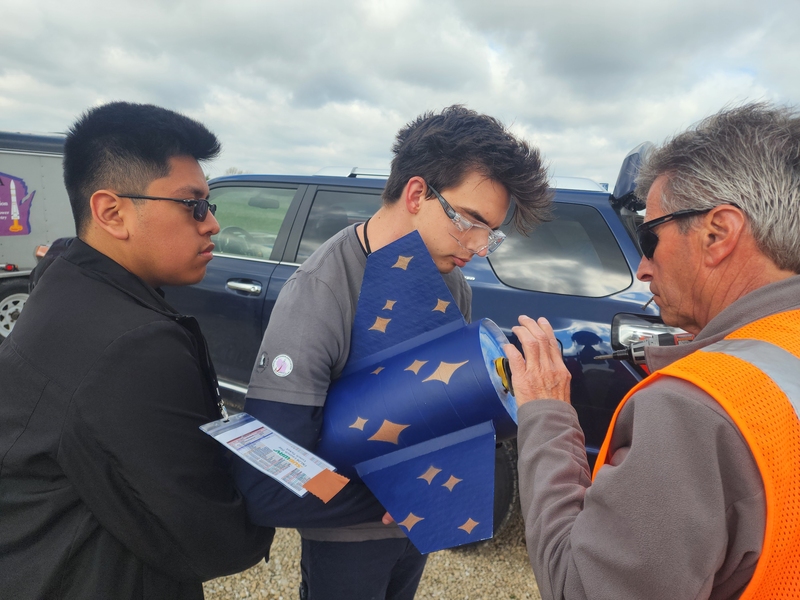 Two students and a race official examine the rocket tail