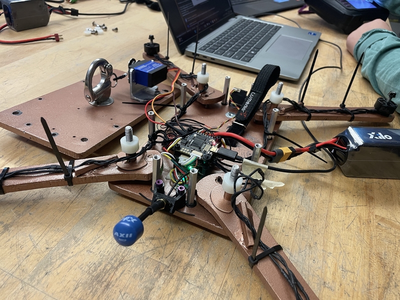 A partially assembled quadcopter drone on a workbench, featuring electronic components, wires, and batteries.