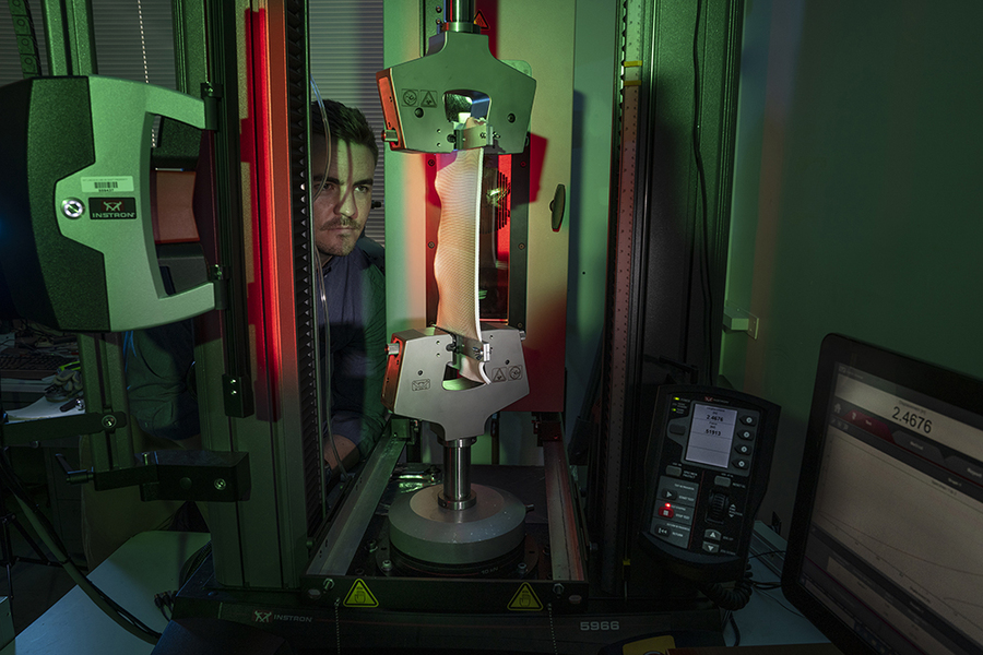 In a darkened room, Steven Gillmer watches a long fabric being stretch-tested in lab equipment.
