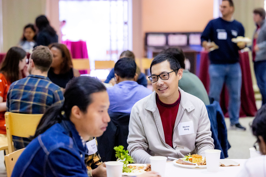 Wenhao Wang smiles while talking with another postdoc at a luncheon.