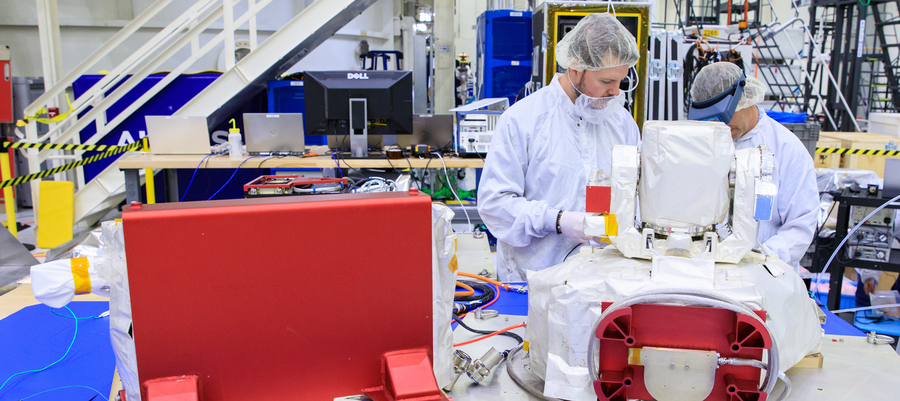Two individuals in cleanroom attire examine an optical communications system payload.