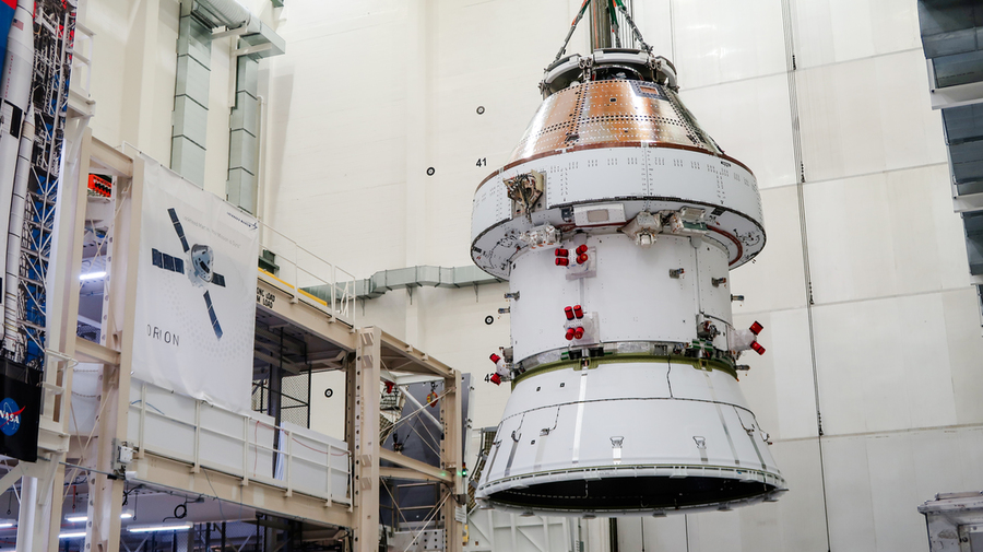 An Orion space capsule with its service module is lifted into a vacuum chamber for testing.