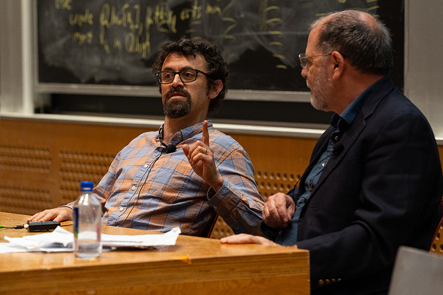 Alexander Gourevitch and Tyler Cowen, seated at a table. Gourevitch raises his index finger while making a point.