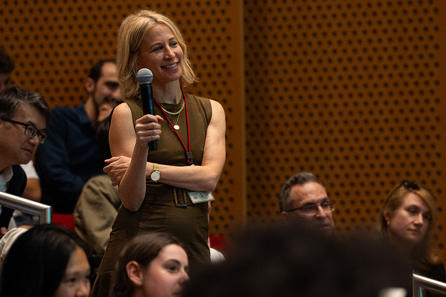 Linda Rabieh, holding a microphone, stands in an audience