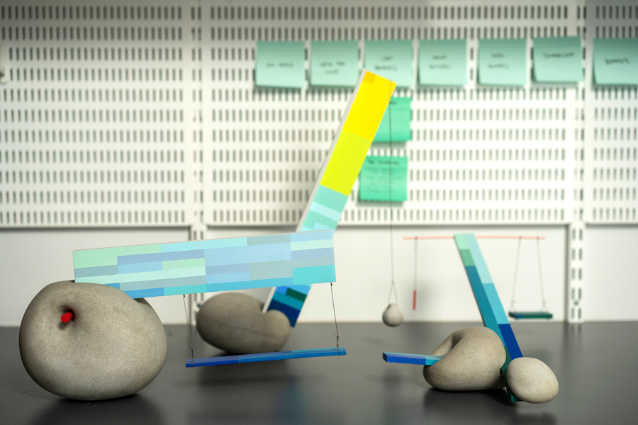 A desktop prototype for a park’s architecture includes smooth stones with blue rectangular roofs and swings.