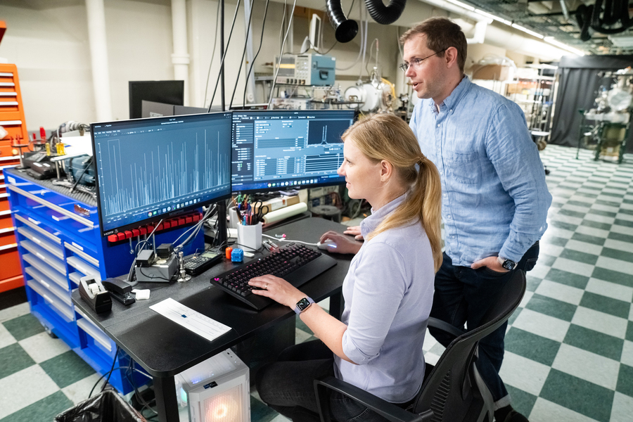 Gabi Wenzel sits at computer in lab and looks at data with Brett McGuire.