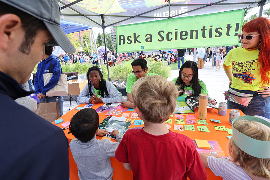 Several people sit at a table under an "Ask a Scientist" banner. Several kids appear before them.