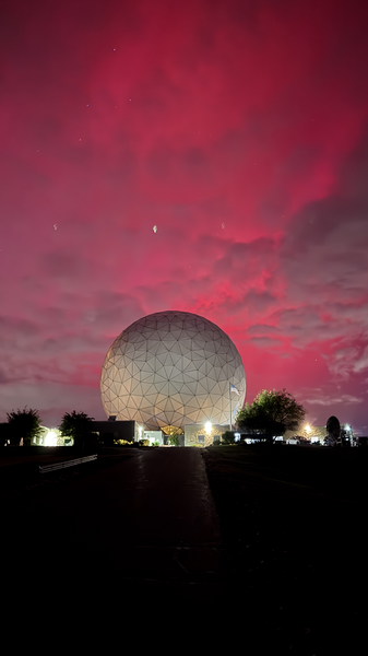 Bright pink aurora behind a large white geodesic dome outside