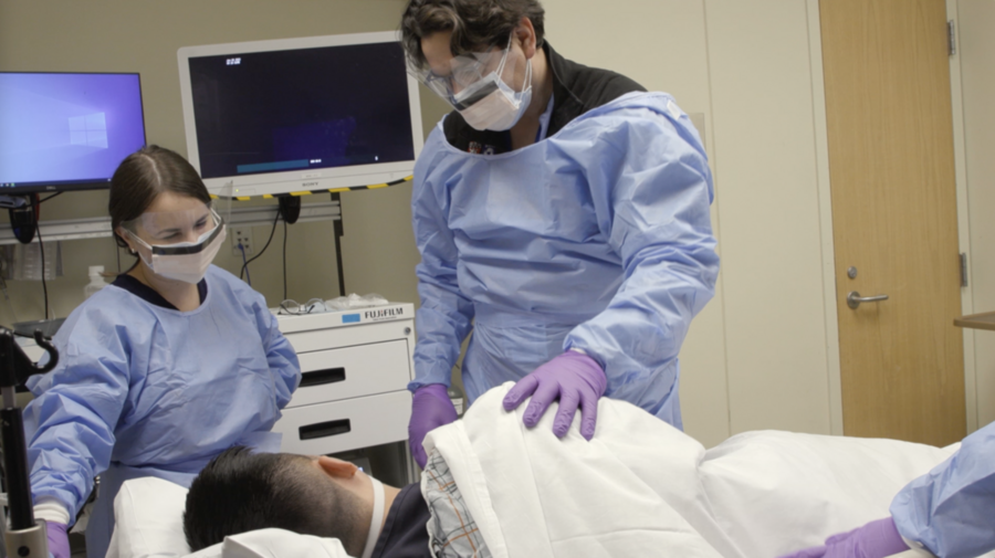 Giovanni Traverso and a student dressed in medical attire attend to a patient in a hospital bed.