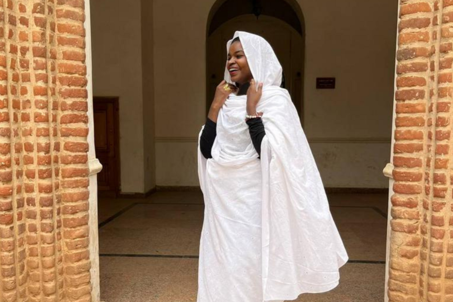 Sujood Eldouma stands in a brick doorway. She is facing slightly away from the camera and smiling.