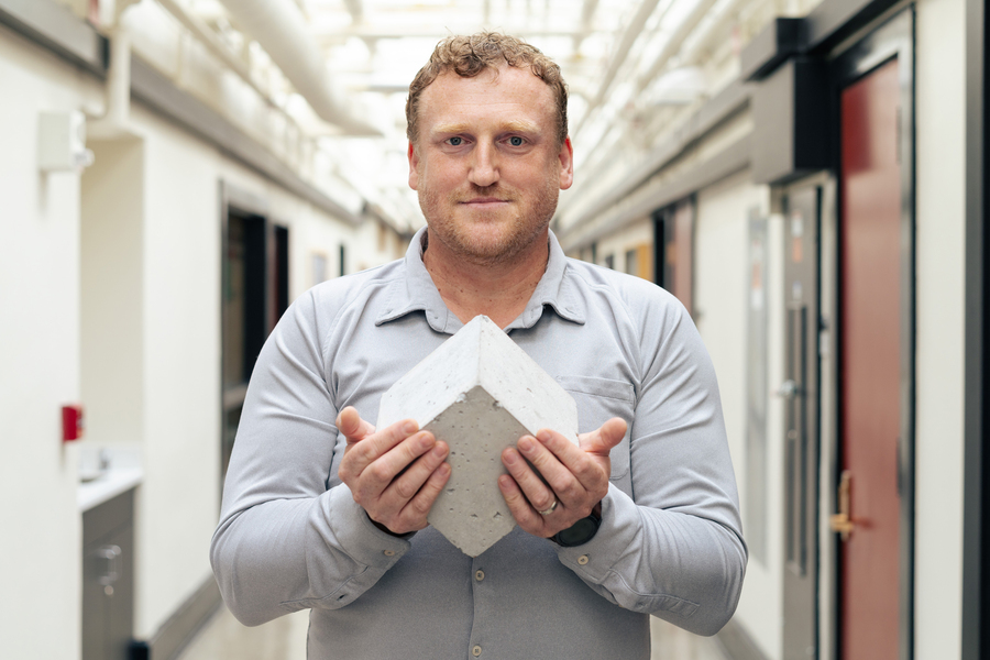 Admir Masic stands in MIT hallway holding a concrete cube.