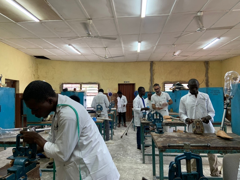 A group of people in white coats work on orthotics at separate tables.