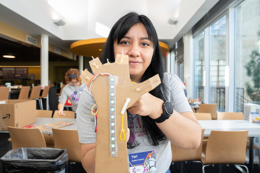 A woman holds a mechanical arm made out of cardboard for the camera's inspection.