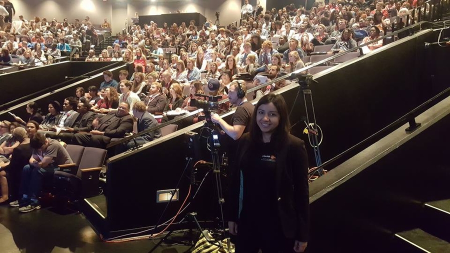 A woman stands next to a large seated crowd.