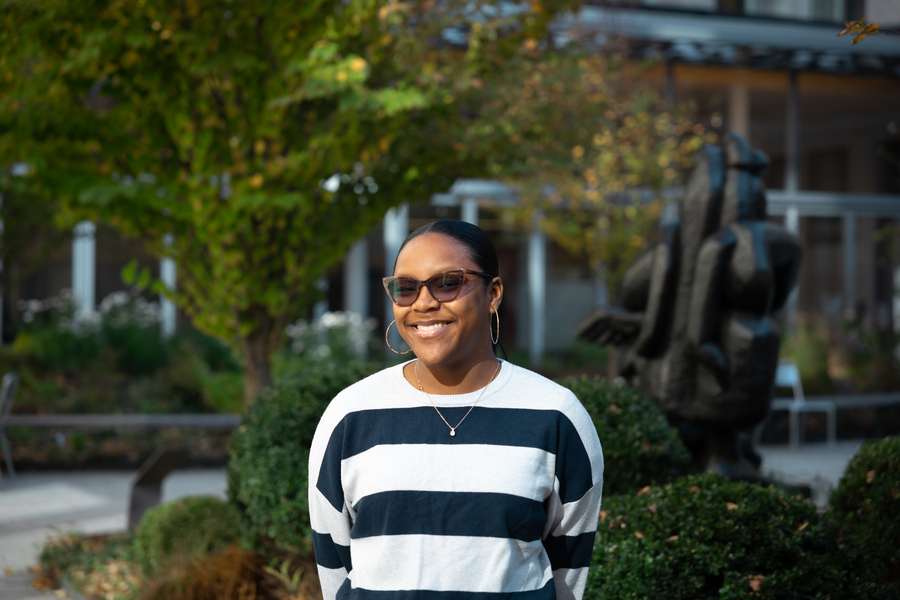 Chenise Harper wears sunglasses and smiles broadly while surrounded by the greenery of the Cambridge campus.