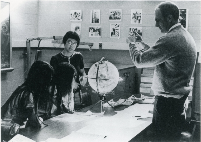 Grayscale photo of a young Hale Bradt in a classroom with three students who are examining a globe.