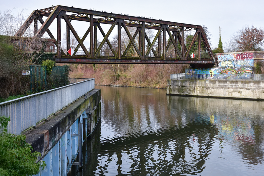 A rusty steel railway bridge spans a calm river.