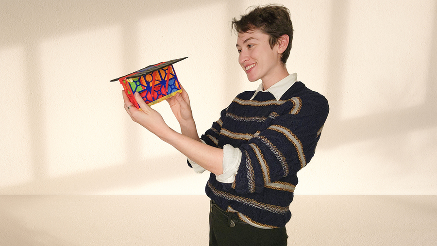 Sydney Dolan holds a 3D-printed satellite model, a bit smaller than a shoebox, in front of a white wall