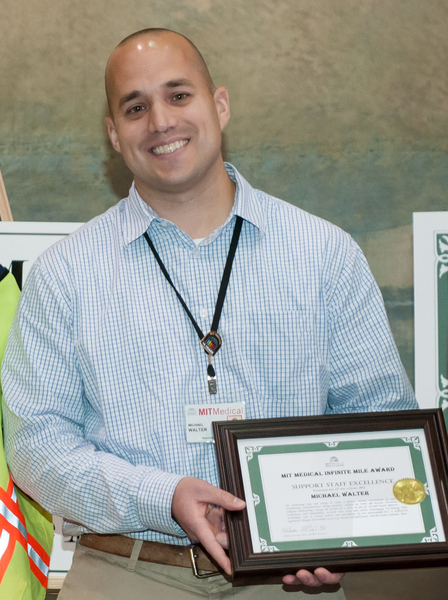 Photo of Mike Walter wearing an MIT Health lanyard and displaying his framed award certificate