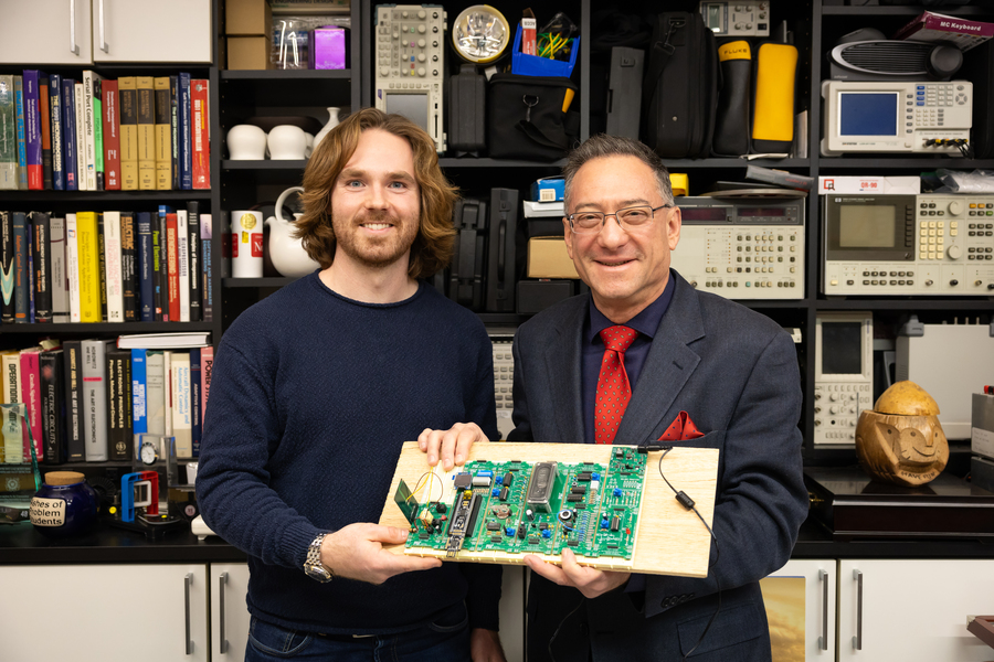 Dan Monagle and Steve Leeb hold a display board showing multiple credit-card-sized circuit boards.