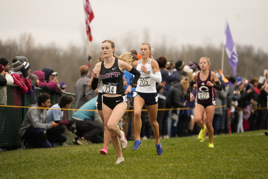 Several women running on a grassy track, with the MIT runner in front