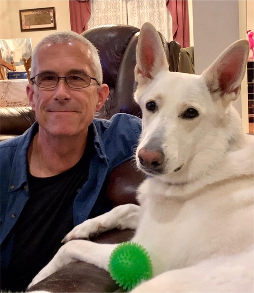 Matthew Dolan sits on a couch with a large white German Shepherd dog