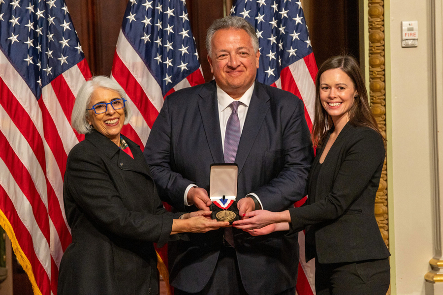Arati Prabhakar, Noubar Afeyan, and Hamilton Bennett pose together with a medal, in front of a U.S. flag