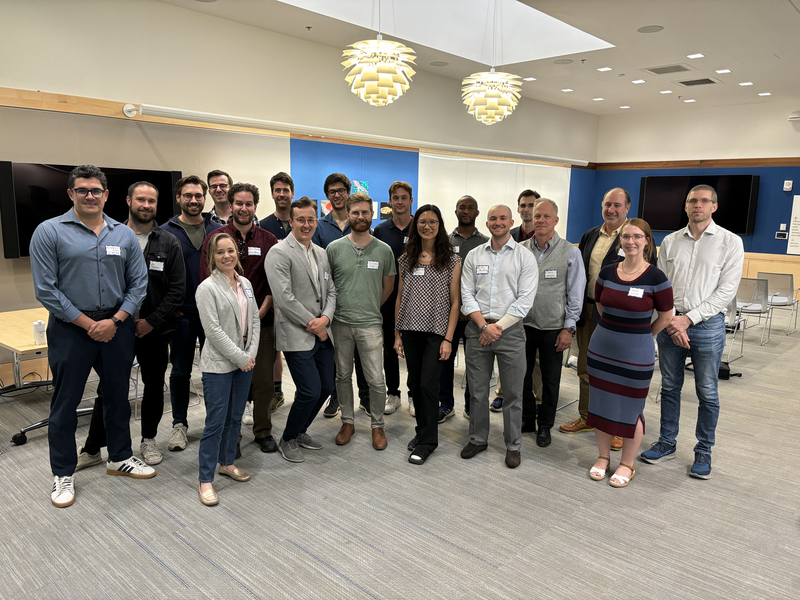 A group of about 20 people pose standing in a classroom at MIT.nano.