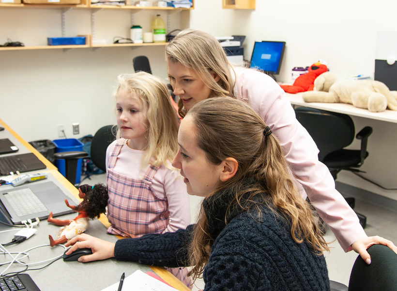 Two women and a young girl look at a computer screen.