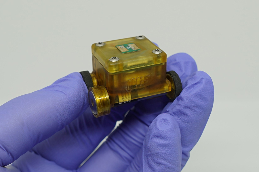 A gloved hand holds a tiny 4-wheeled rover.