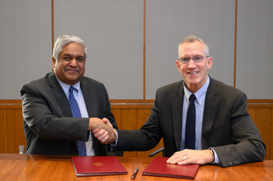Anantha Chandrakasan and Gregg Bartlett, both in suits, sit at a table and shake hands for the camera