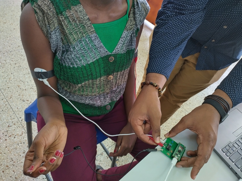 The arms and torsos of two people are shown with an EKG device being tested on one person's arm