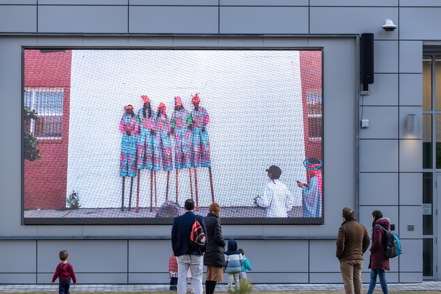 Passersby view a large image projected onto a building wall outdoors