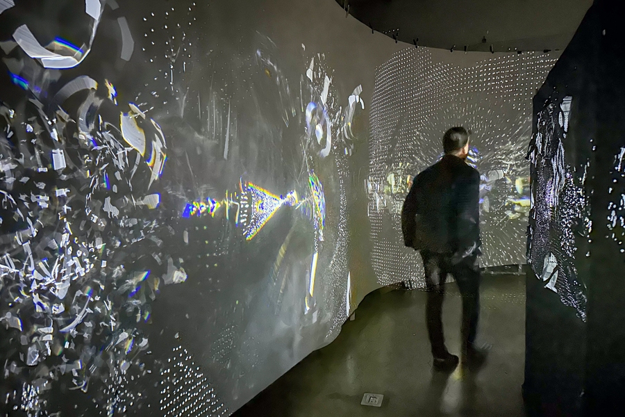 A man walks down a hallway with lights and shapes projected on the walls