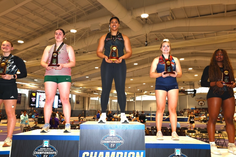 Alexis Boykin stands atop a five-tier NCAA Championship podium inside a field house; each winner holds a trophy.