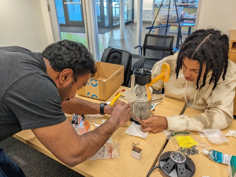 Two class participants build an autonomous underwater vehicle from parts spread on a table in front of them