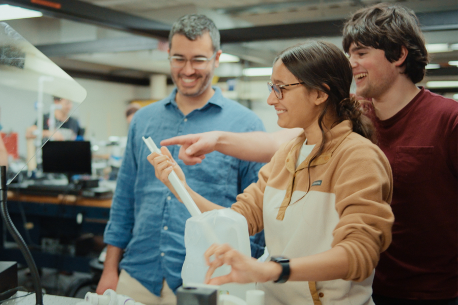 Three people in a workshop setting examine a white object.