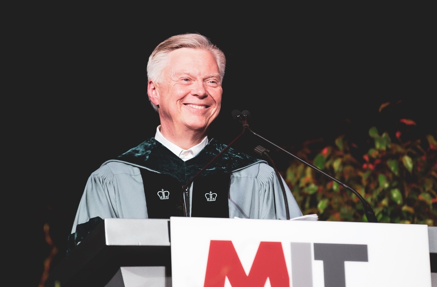 David Schmittlein wearing Commencement regalia and smiling at a lectern