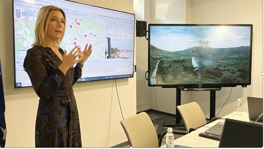 Mirnesa Softić speaks in front of two screens displaying a map and wildfire. 