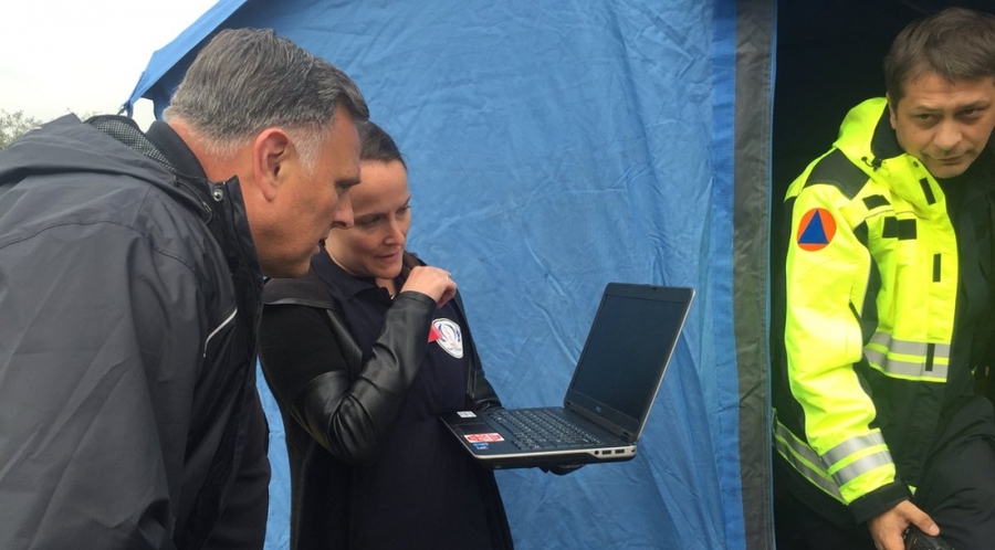 Stephanie Foster and William Bryan, stand outside a tarp tent, looking at a laptop.