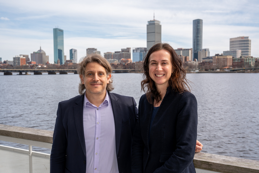 Themis Sapsis and Fotini Christia pose together in front of the Charles River, with Boston’s skyline in the background
