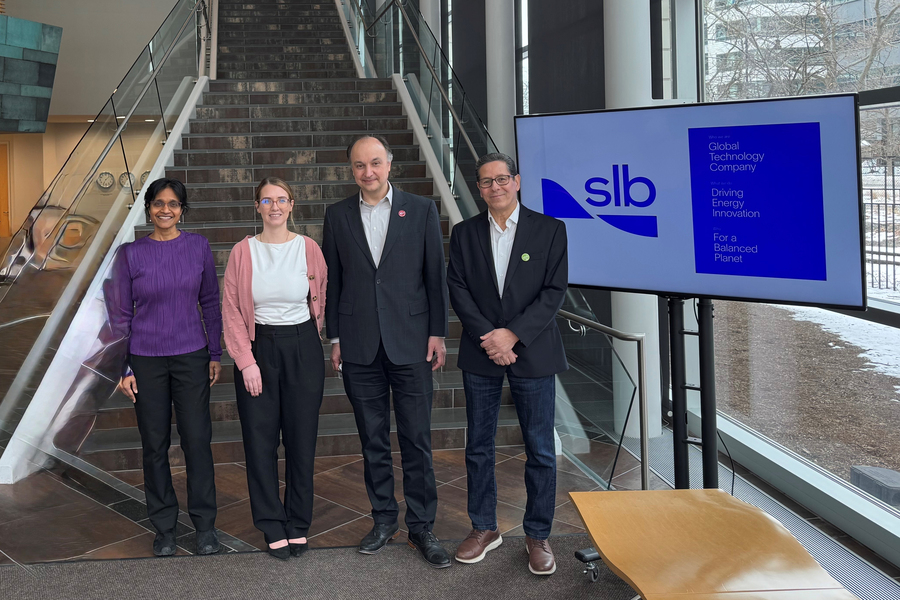 Four people pose in front of a staircase and a screen that says "SLB"