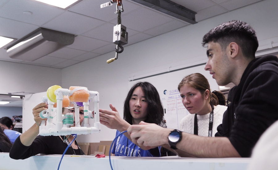 Karen Guo gestures at a SeaPerch robot while three high school students look on