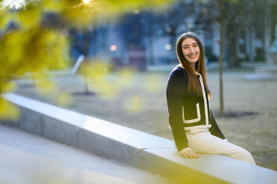 Shaylin Cetegen sits on a stone wall with foliage in foreground